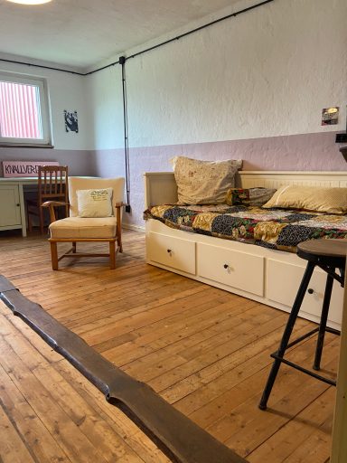 Ein einfach eingerichteter Raum mit einem Bett, Stuhl und Holzfußboden.
