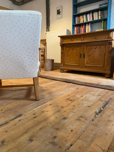 Stuhl und Holzfußboden, mit einer Kommode und Büchern im Hintergrund.