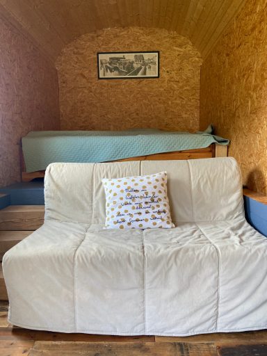 Gemütliches Sofa mit Kissen in einem Raum mit Holzvertäfelung und einem Bett im Hintergrund.