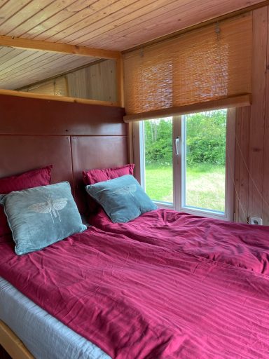 Gemütliches Schlafzimmer mit rotem Bettzeug und Fensterblick auf die grüne Landschaft.