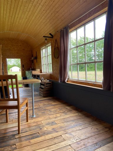Heller Raum mit Holzboden, Tisch, Stuhl und großen Fenstern zum Garten.